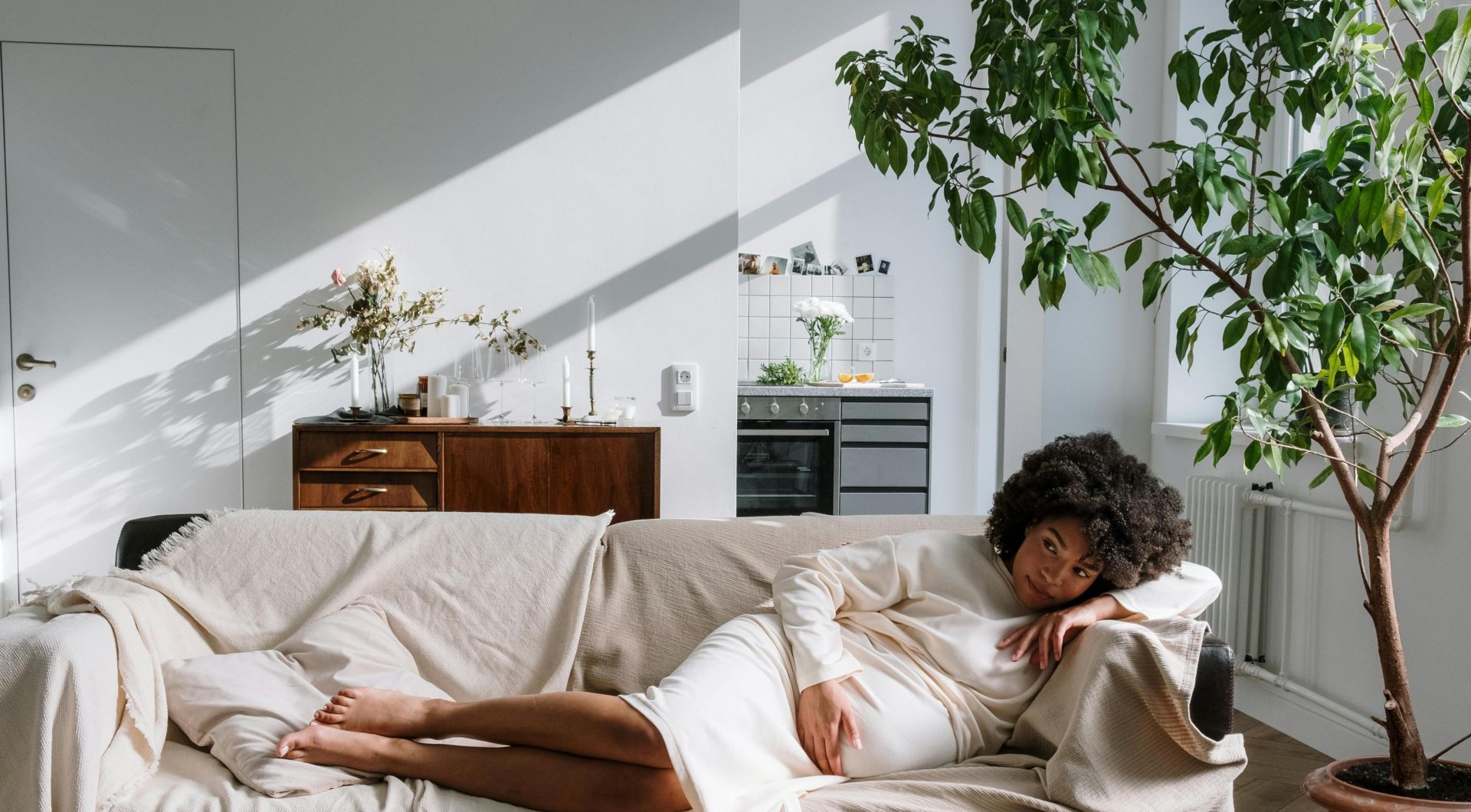 Pregnant woman relaxing on a sofa in a warm, Scandinavian-style living room, bathed in natural light.