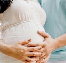 Close-up of hands gently embracing a baby bump in a warm, serene setting.
